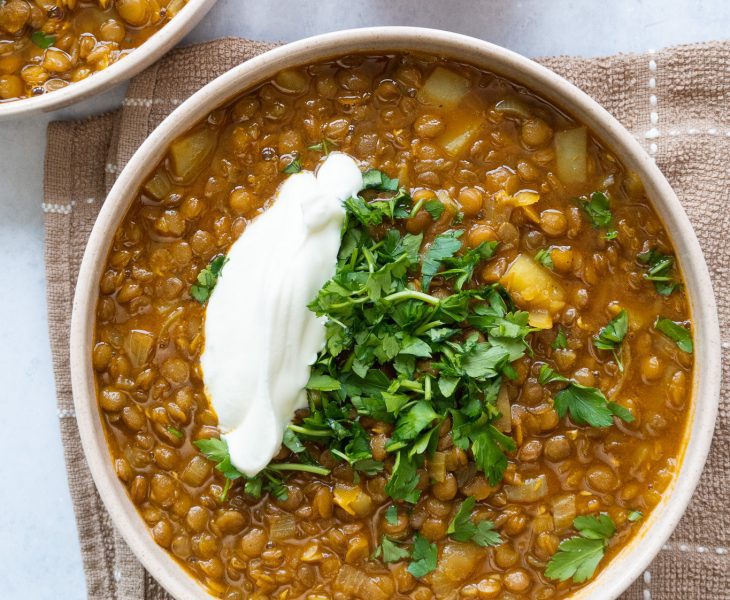 A steaming bowl of Adasi, a flavorful Persian lentil soup, served with a yogurt and topped with chopped herbs. The soup is a warm, comforting mix of lentils, onions, tomatoes, and spices, and is a popular dish in Iranian cuisine.