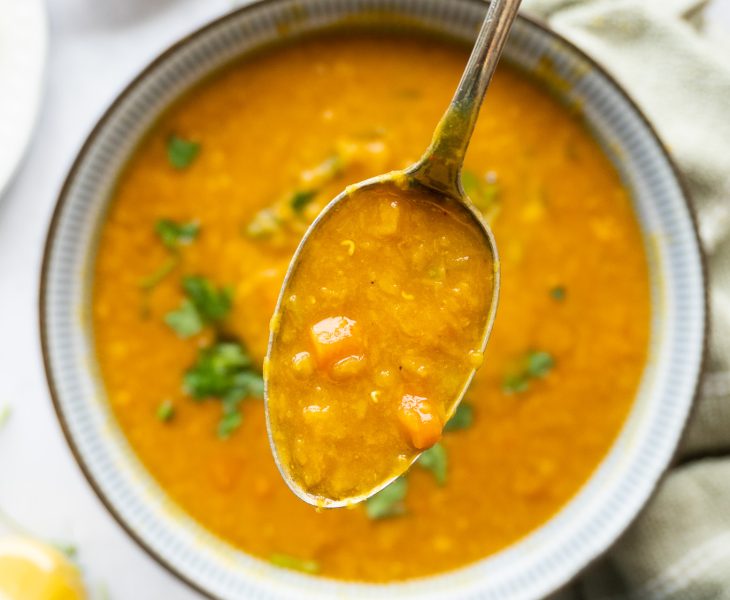 A spoon full of hot turkish lentil soup with garnishing of parsley and lemon slices