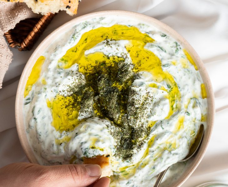 A bowl of Borani Esfenaj - Persian spinach yogurt dip a delicious and healthy Persian dip made with yogurt, spinach, and aromatic herbs. The dip has a vibrant green color and is served with crispy pita chips on the side.