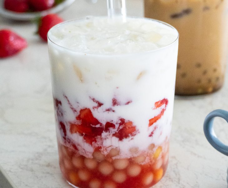 Image of two glasses filled with Easy Homemade Bubble Tea - Korean Strawberry Milk and Brown Sugar Boba with a Shot of Coffee - with tapioca pearls and ice cubes, next to a clear plastic cup with a wide straw.