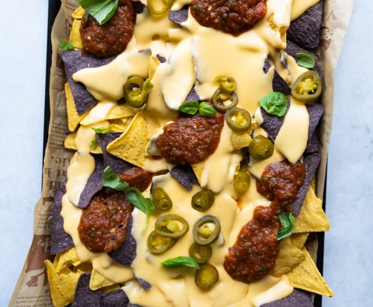 Classic Nachos with Homemade Cheese Sauce - Irresistible Golden and purple corn tortilla chips loaded with homemade cheese sauce, jalapeños, and fresh toppings.