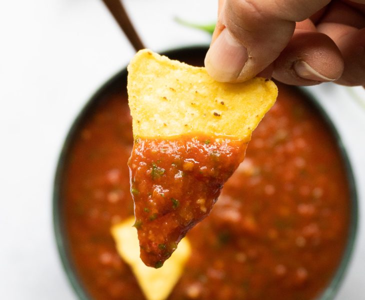 An enticing image of homemade tomato salsa, replicating the famous Costco recipe. Ripe tomatoes, onions, garlic, and aromatic spices create a harmonious blend of textures and tastes. sat on a tortilla chips dipped in salsa